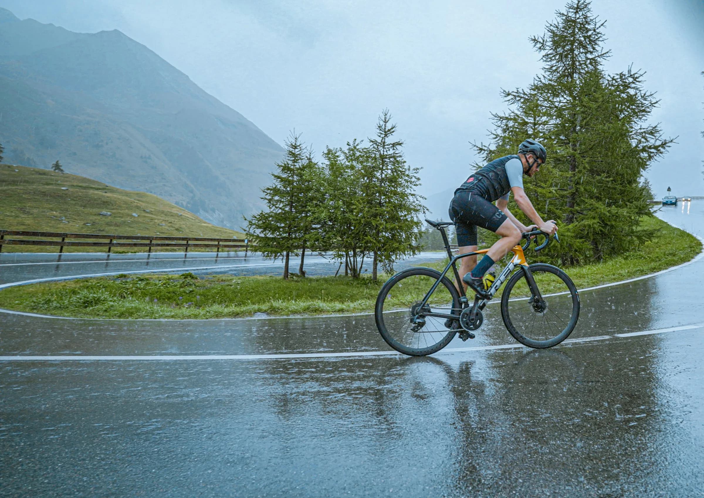 A cyclist on a road bike riding through a bend on a rain-soaked mountain road