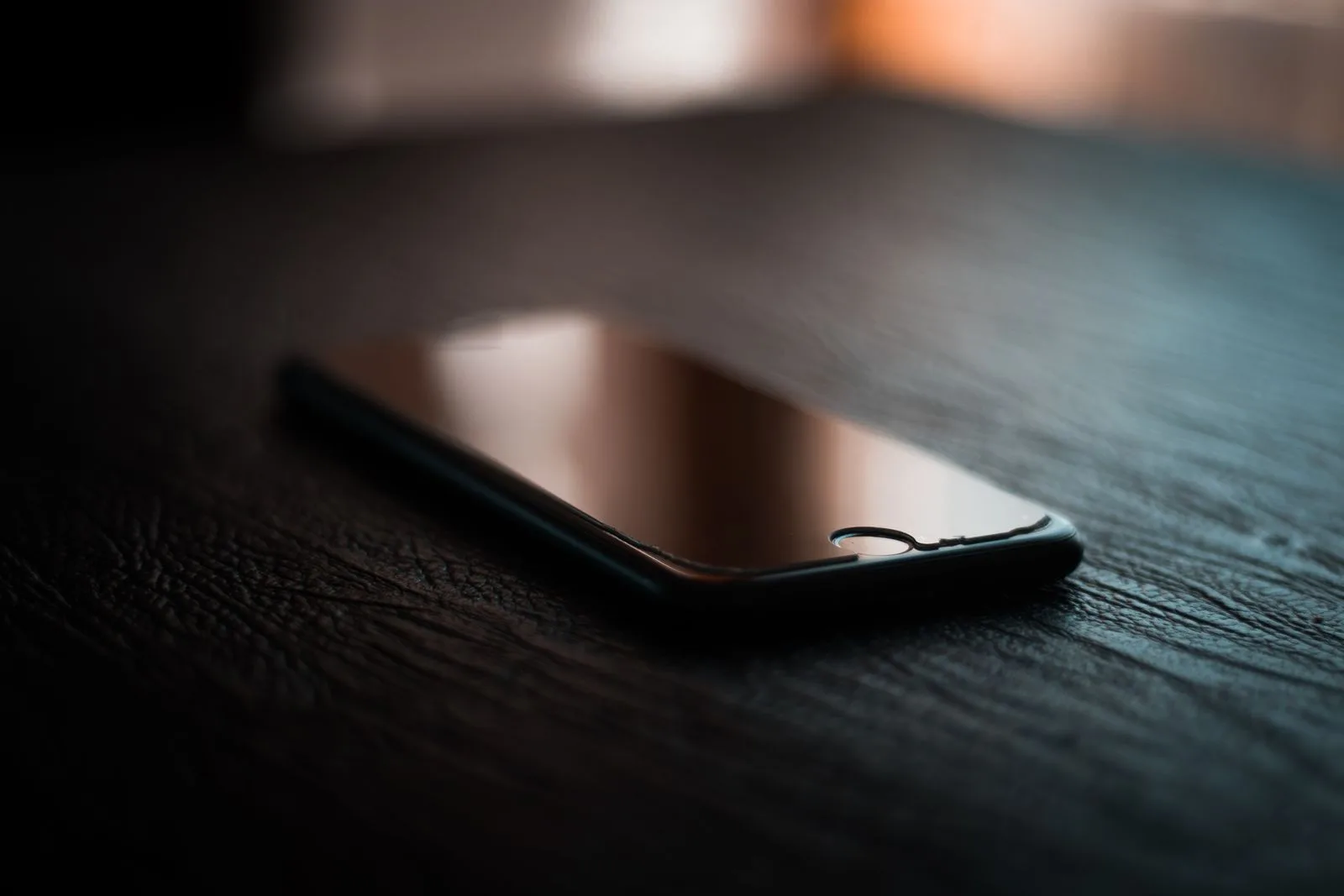 A switched-off phone lying face up on a dark wooden table in low evening light