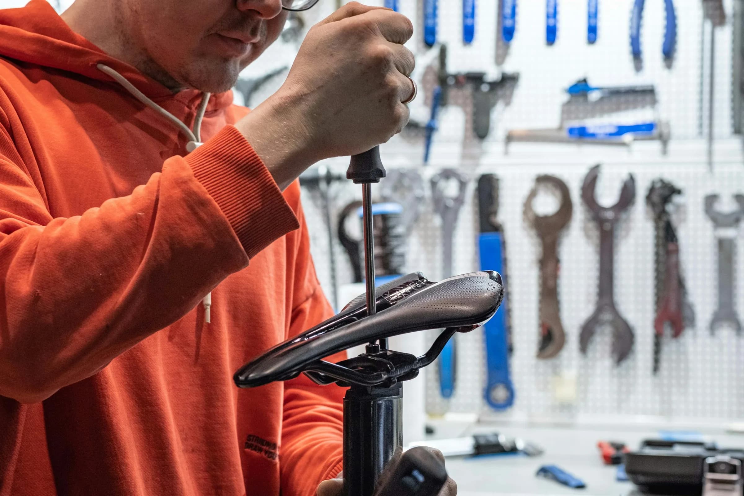 A mechanic adjusting a bike saddle with a hex key in a bike shop