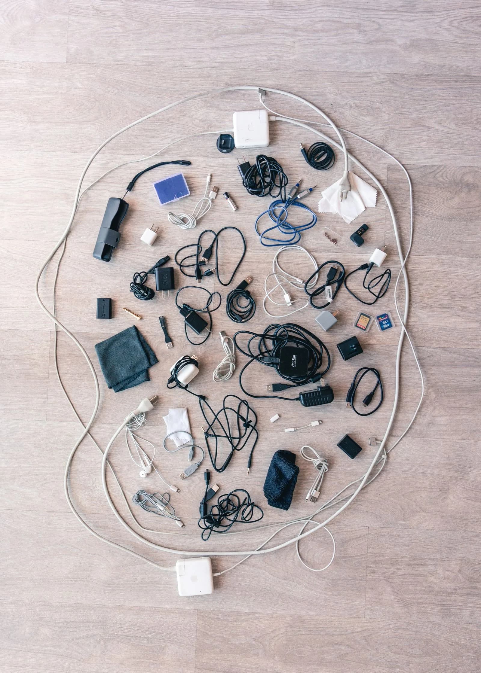 An overhead flat lay of chargers, adapters and cables arranged on a pale wooden floor