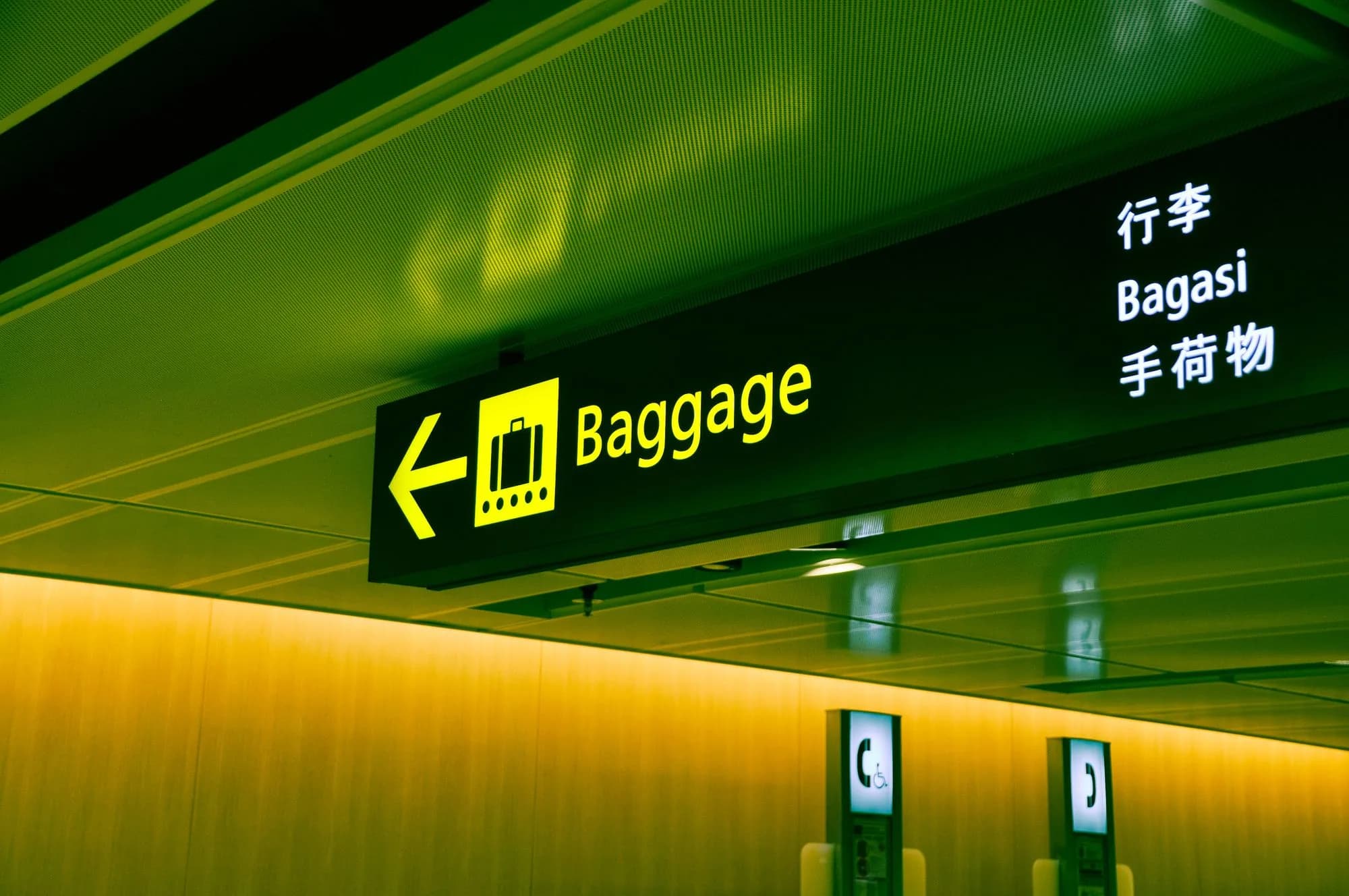 A lit Baggage sign with an arrow hanging from an airport ceiling