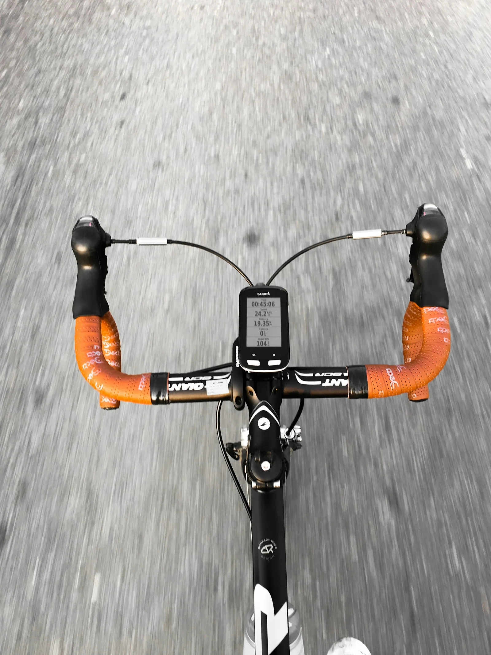 A road bike computer on drop handlebars showing speed and average speed while riding on a paved road