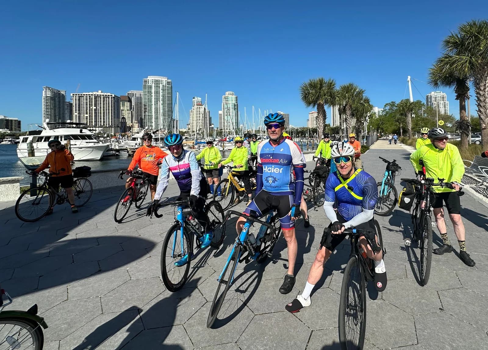 The group lined up on a waterfront promenade at the start of a morning ride, city skyline behind