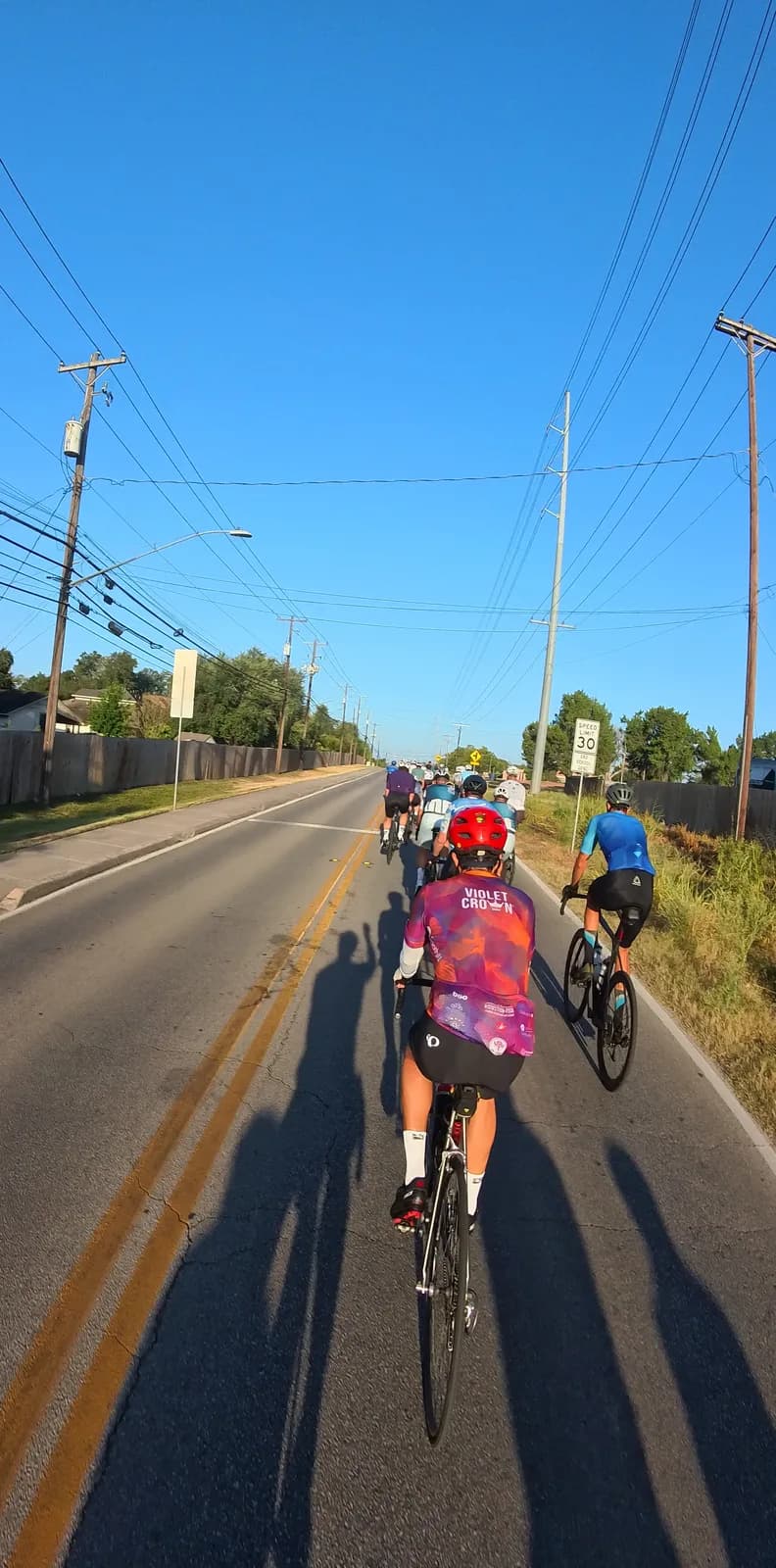 Three riders ahead on a sunny morning road, long shadows across the lane
