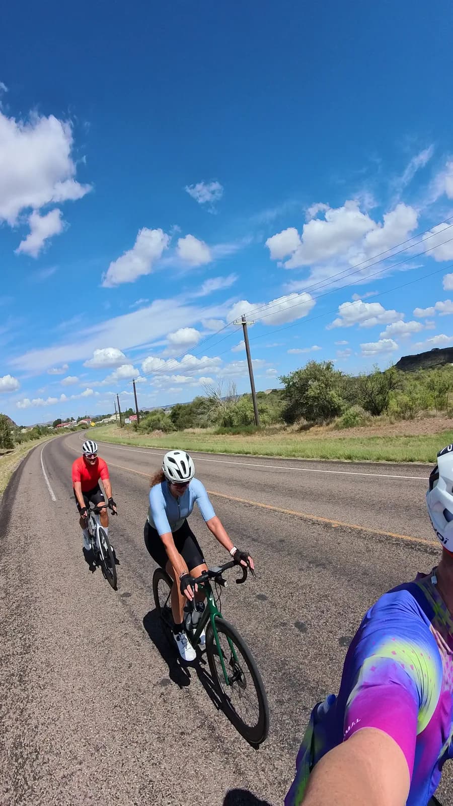 Two riders waving on an empty desert highway under big clouds