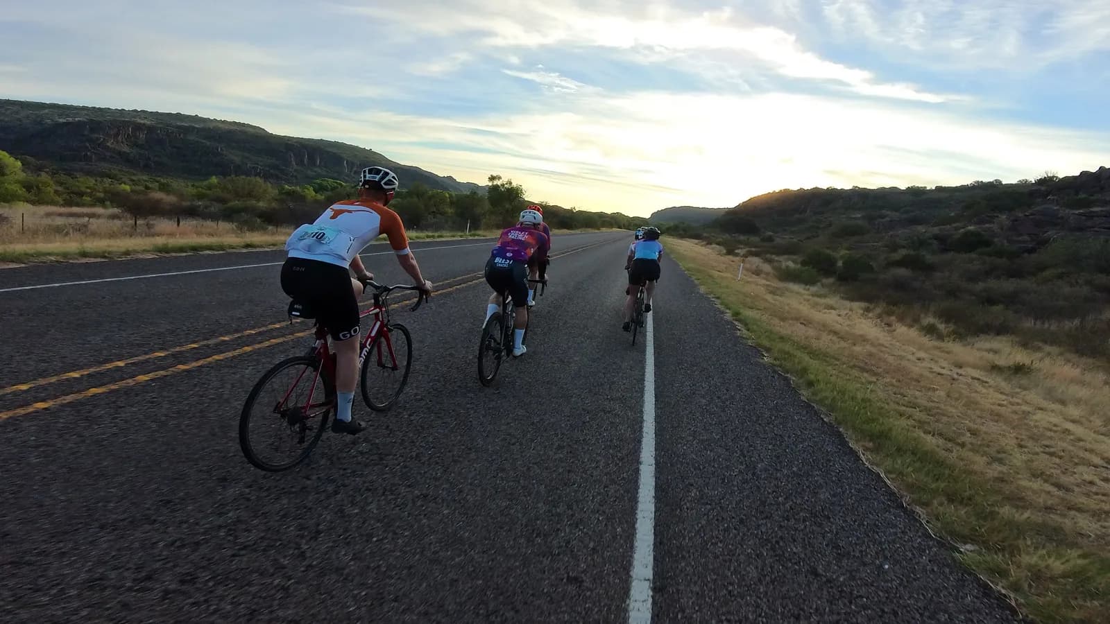 Three riders on a desert highway at sunset, mountains on the horizon