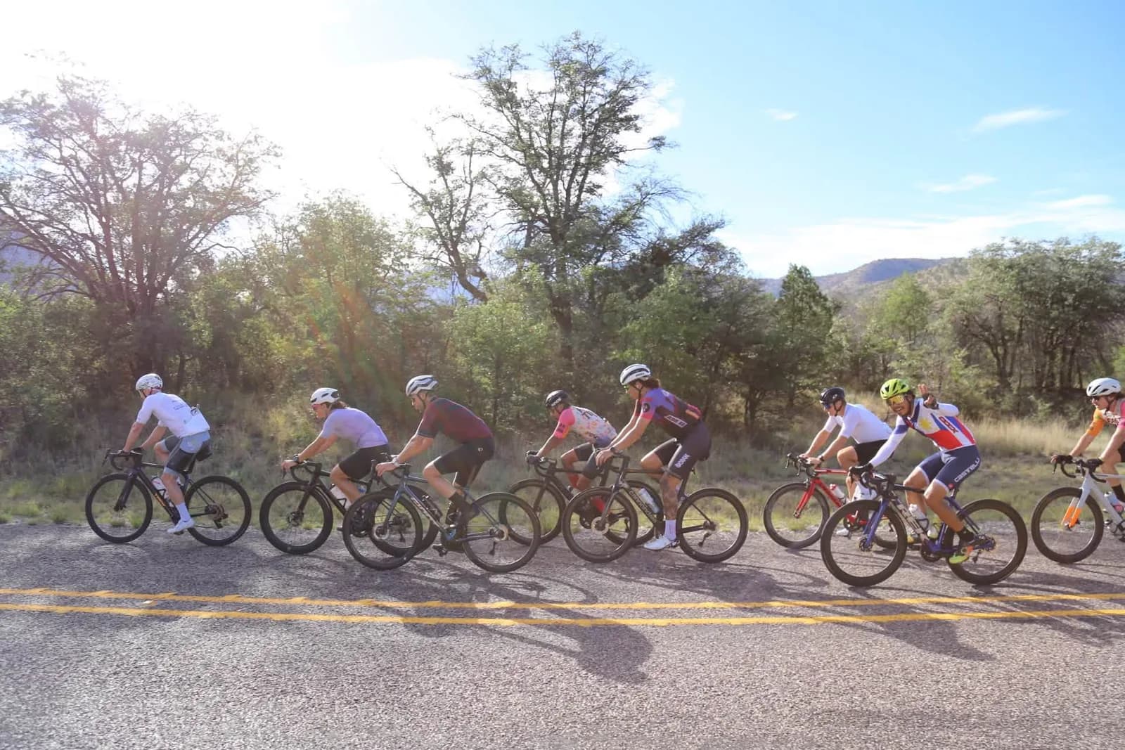 A paceline through wooded hills, the sun flaring through the trees