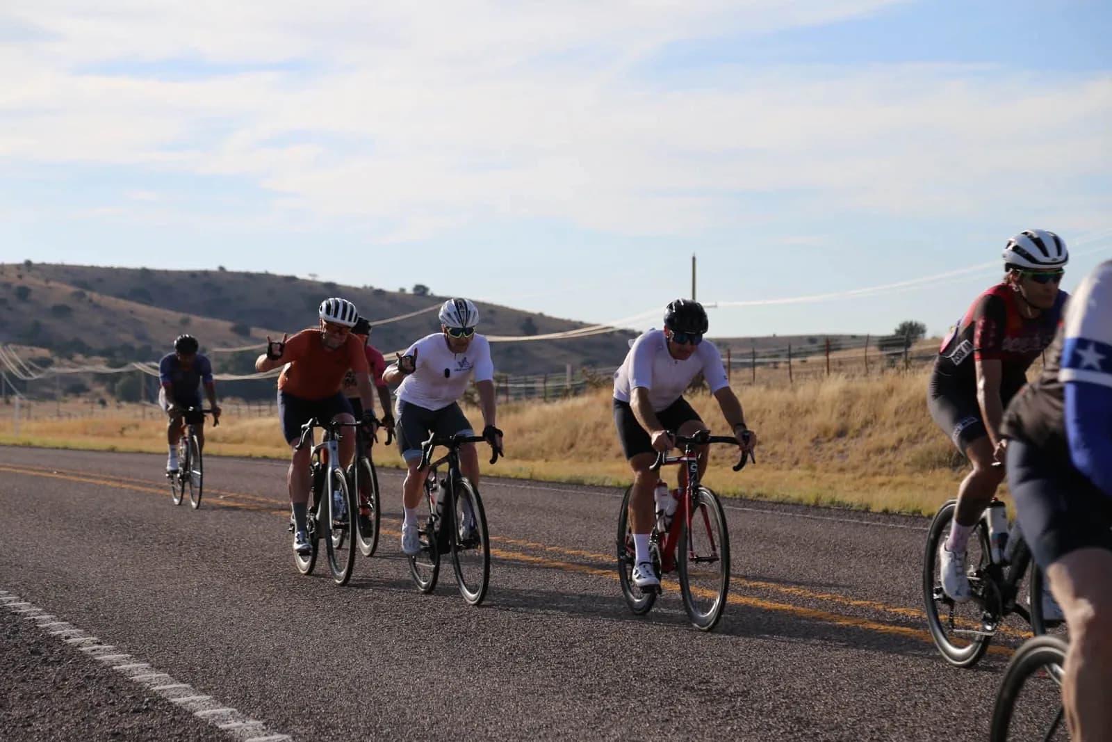 Riders sweeping past on an open highway, low hills behind